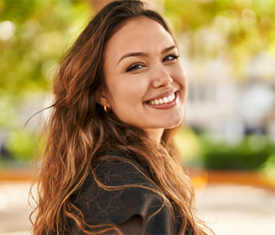 Brunette woman smiling over her shoulder on a sunny day